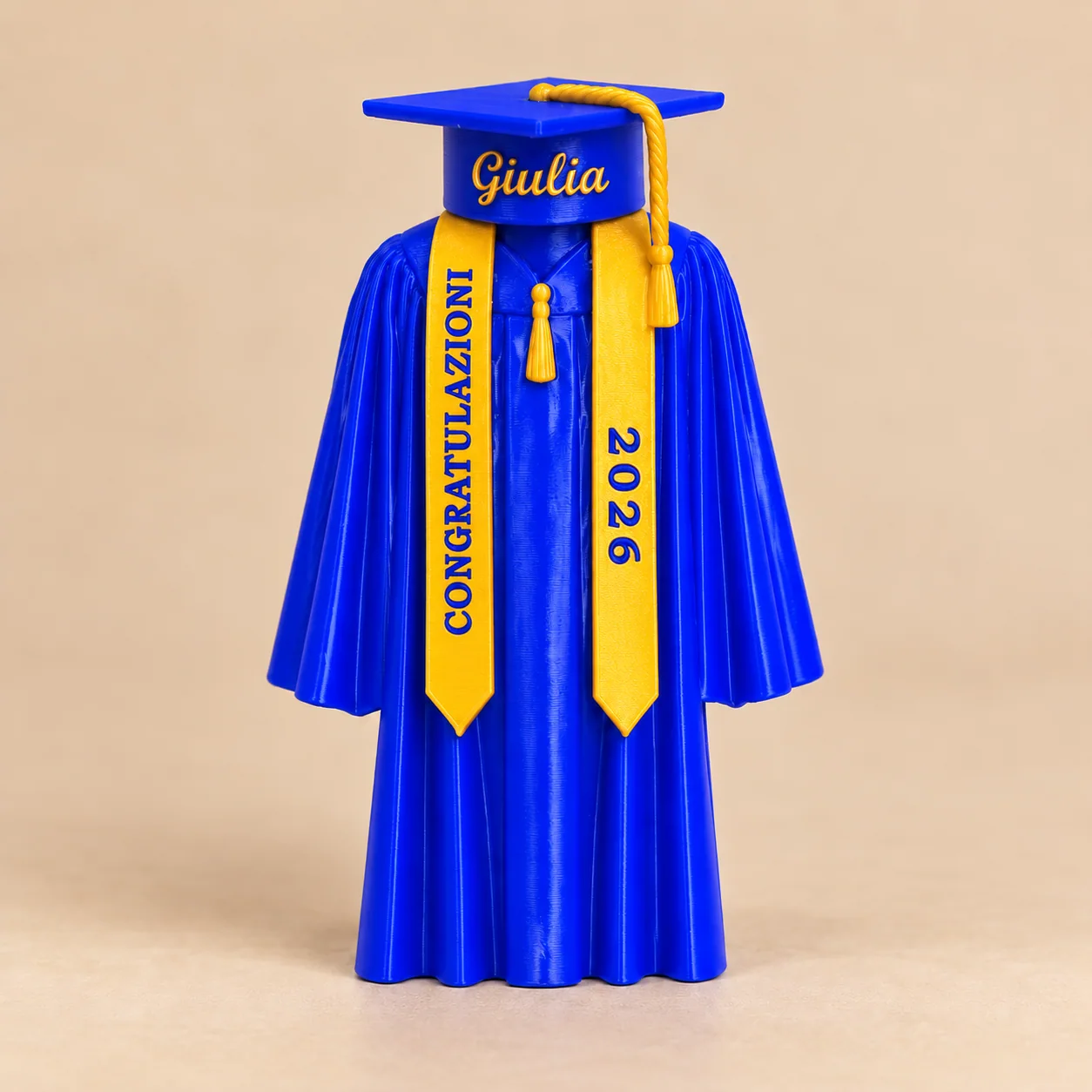 Esempio illustrativo di tocco e toga blu e oro con Giulia e scritte CONGRATULAZIONI e 2026 ruotate lungo la stola, su sfondo beige neutro
